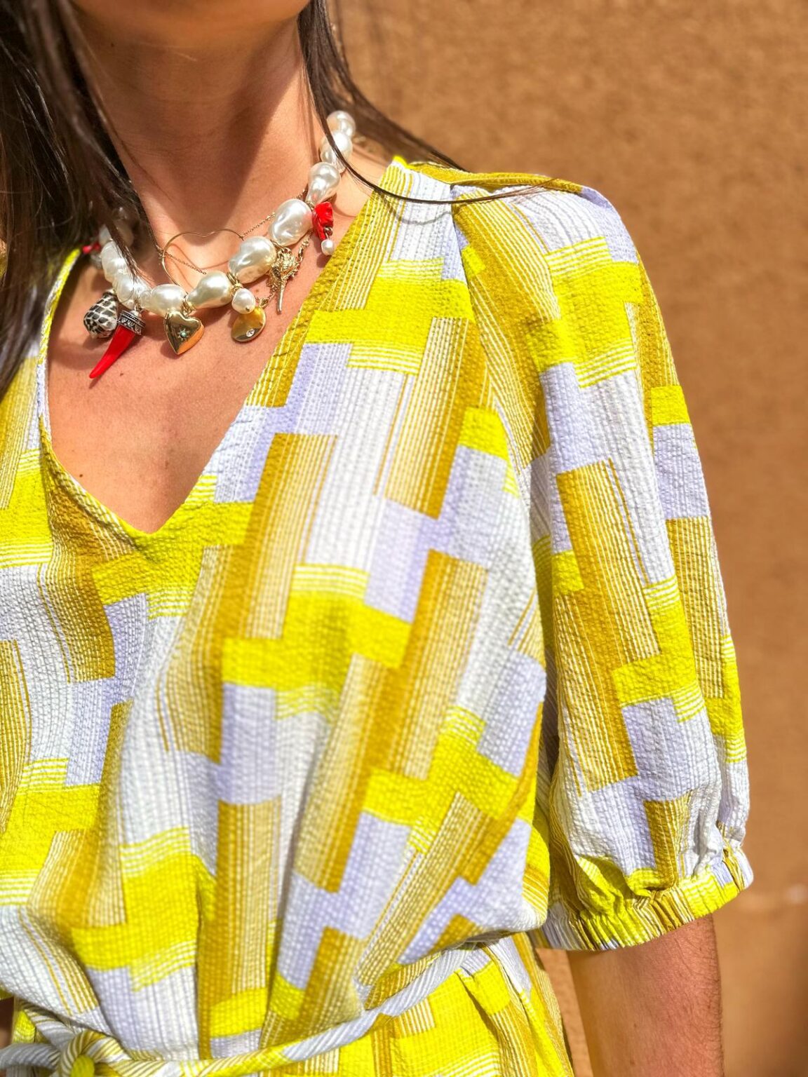 Robe à motifs géométriques jaunes et blancs avec un collier de perles, disponible à la boutique Mademoiselle K à Cassis. Parfaite pour un look estival chic.